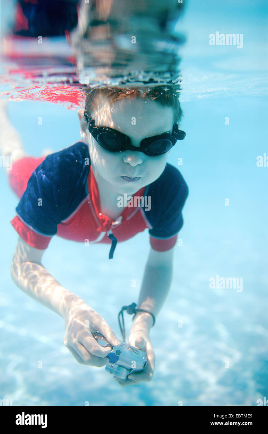 little boy wearing swimming goggles diving with an underwater camera in