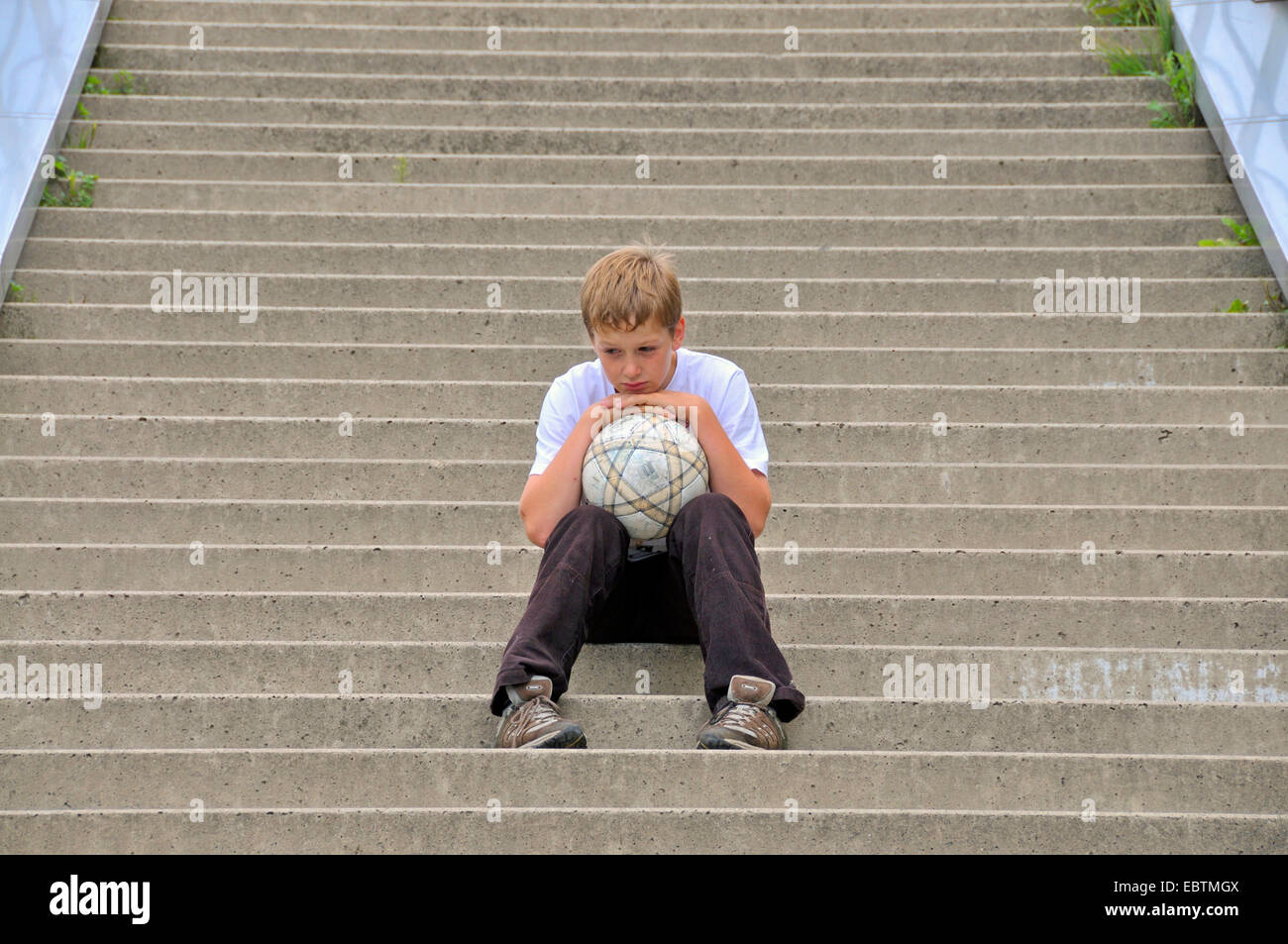 lonesome ten years old boy sitting on stairs with a football, Germany