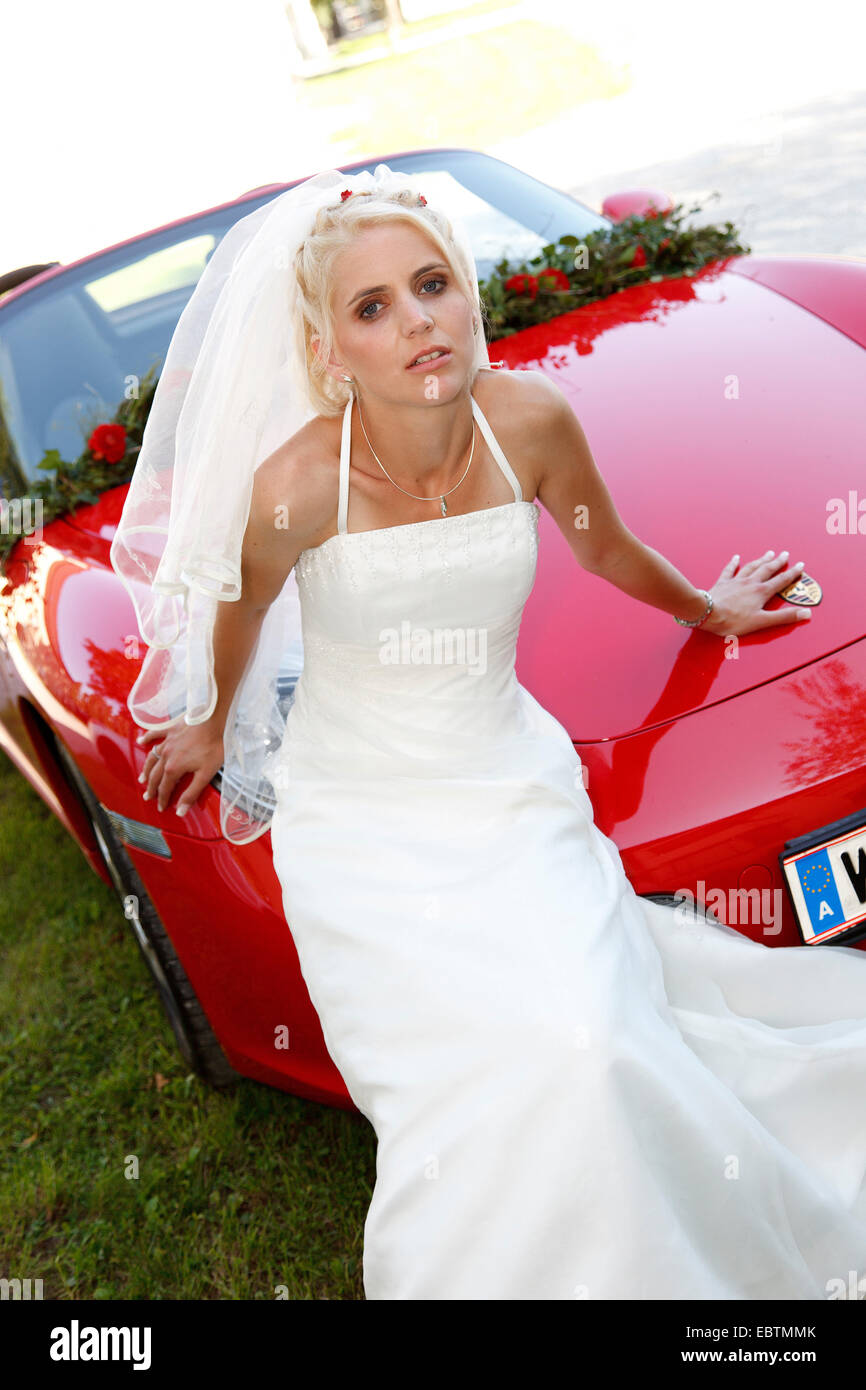 bride posing in front of a red convertible sports car Stock Photo