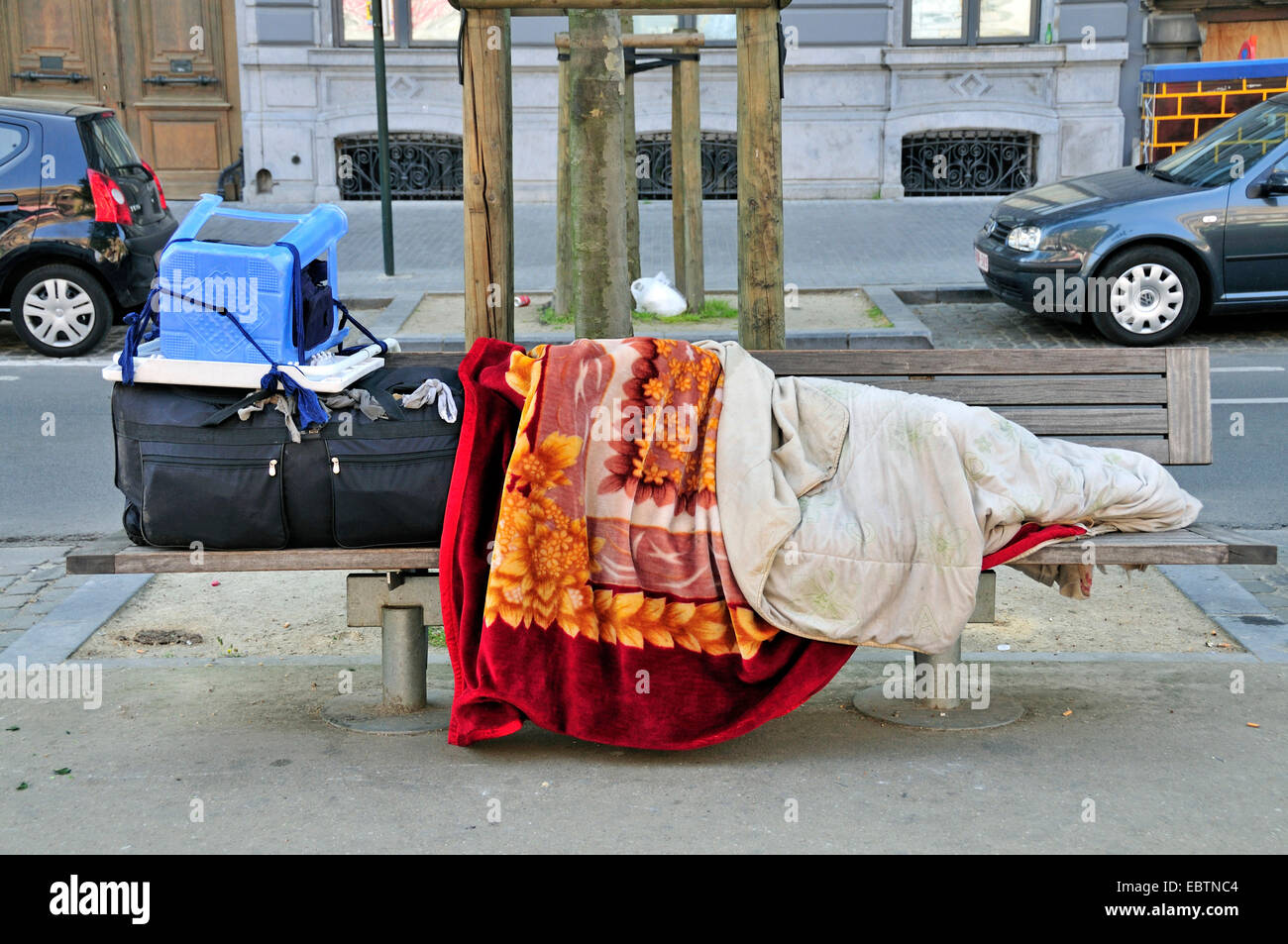 homeless person covered with blankets, sleeping on park bench, Belgium