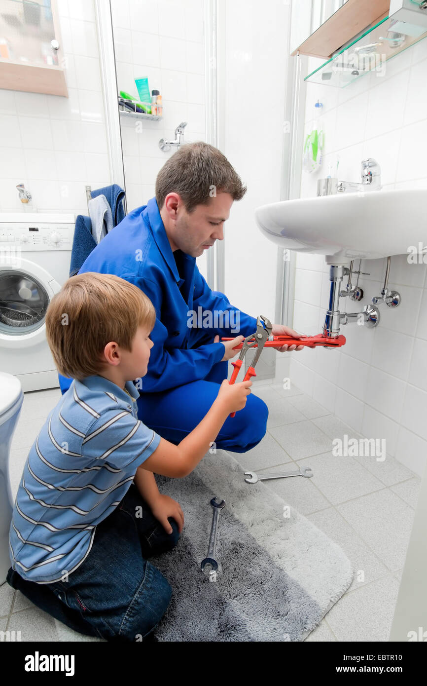 plumber repairs sink in bathroom, boy helpig him Stock Photo