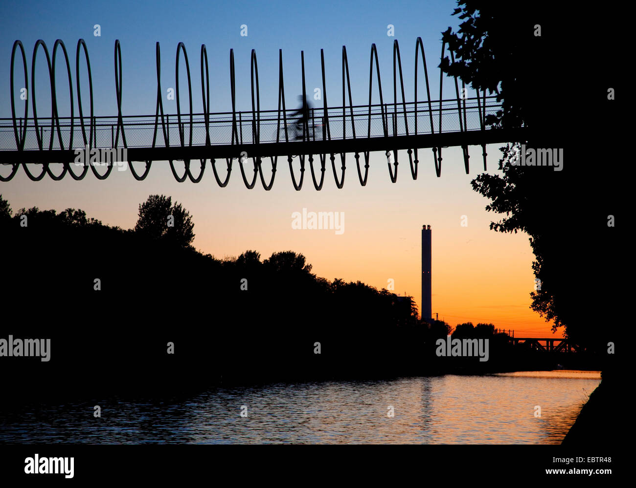 biker on the Slinky Slinky Springs to fame at sunset bridge over Rhein Herne Channel, Germany, North Rhine-Westphalia, Ruhr Area, Oberhausen Stock Photo