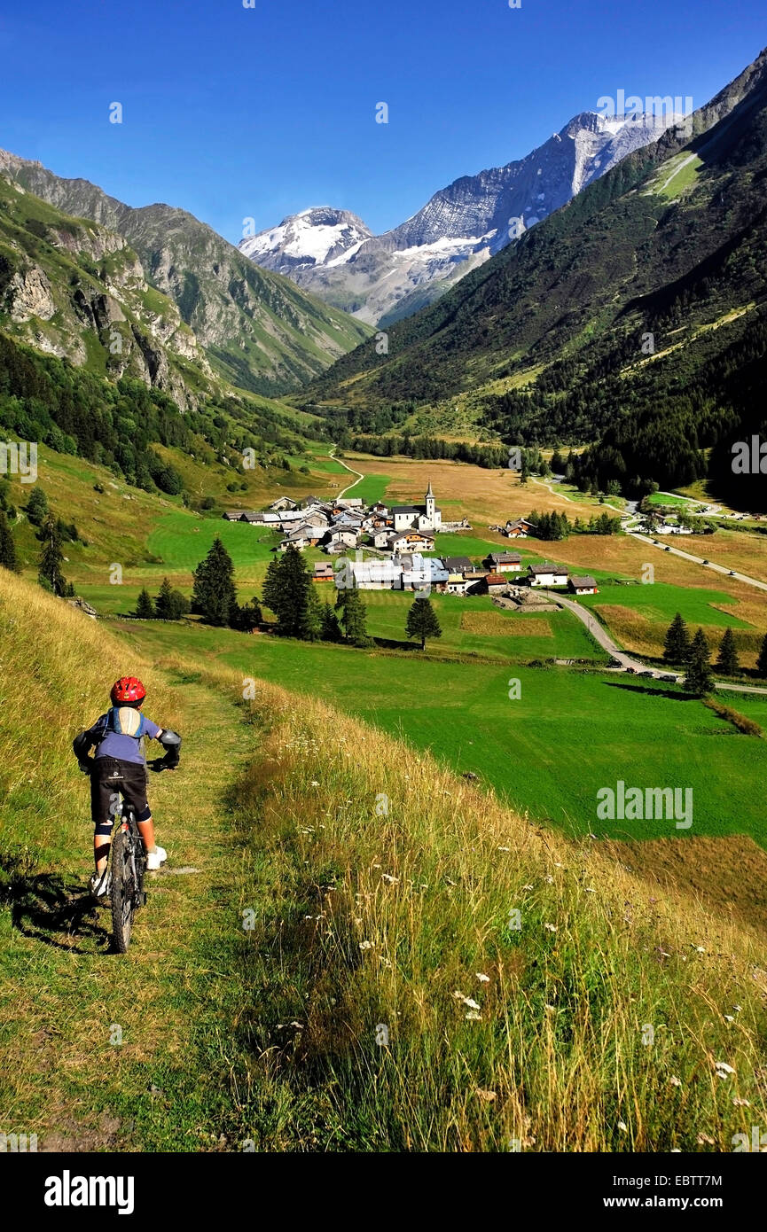 young mountain biker driving through mountain meadow to idyllic valley, France, Savoie, Champagny en Vanoise Stock Photo