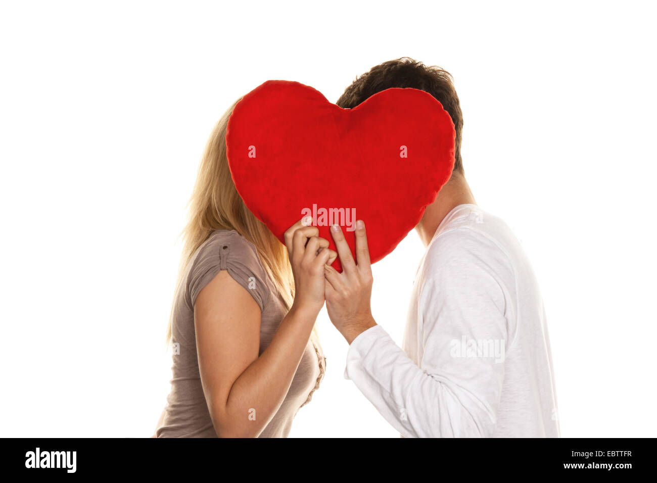 couple in love hiding and kissing behind a heart-shaped red cushion Stock Photo