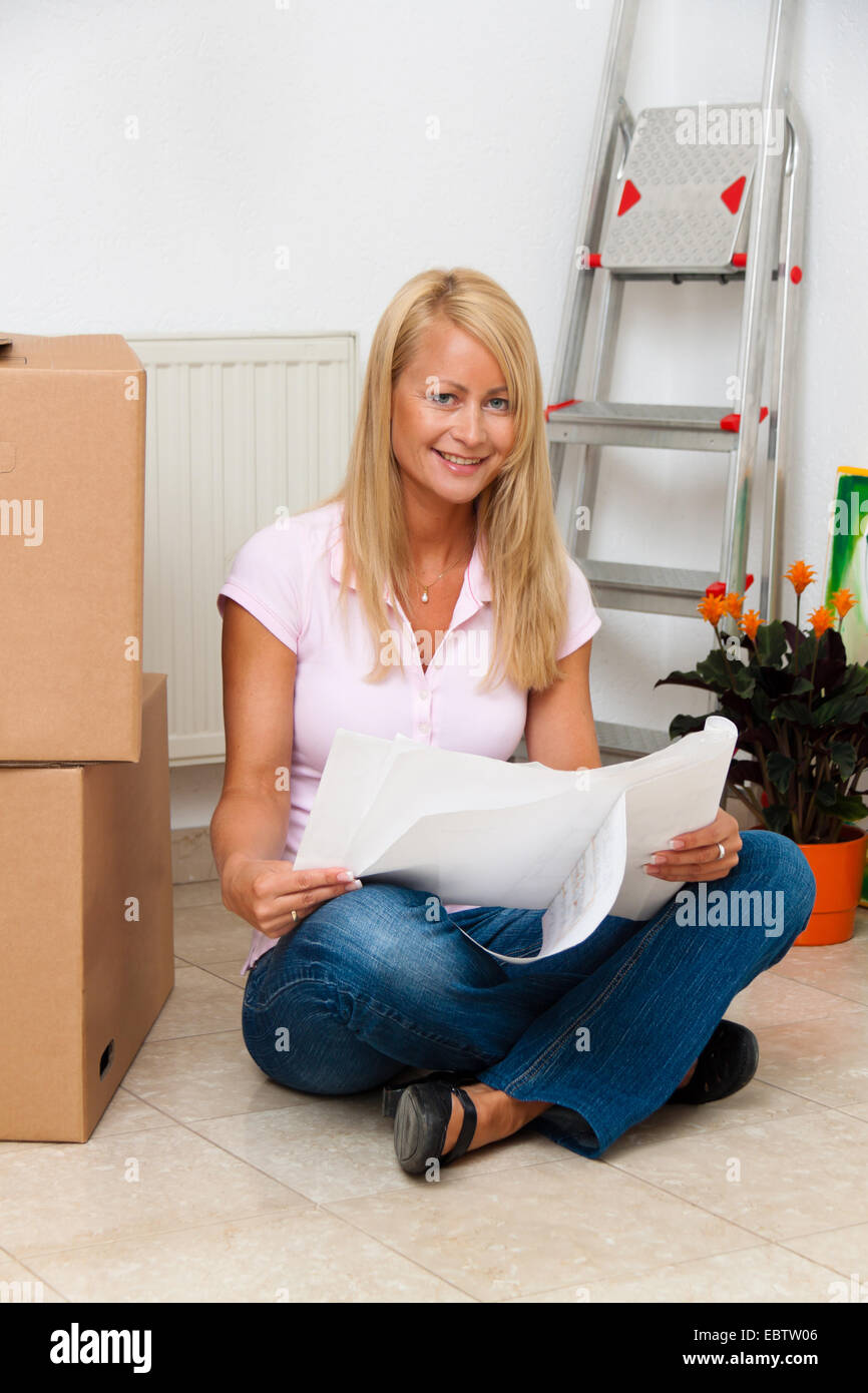 young woman happily sitting on the floor of her new flat beside moving box Stock Photo