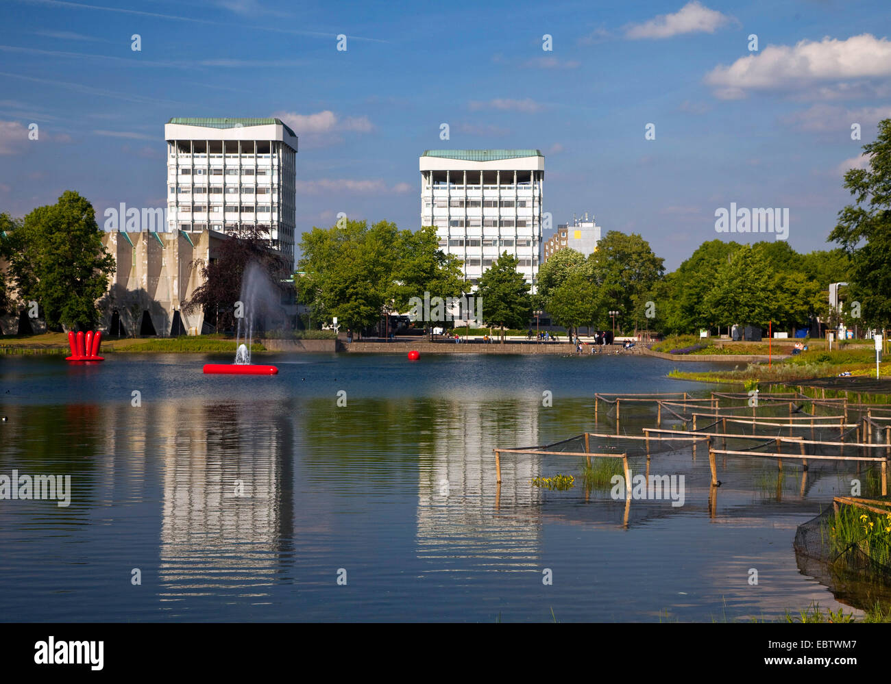 two young people sitting on a bench at the city lake with the two town hall towers in the background reflecting in the water, Germany, North Rhine-Westphalia, Ruhr Area, Marl Stock Photo