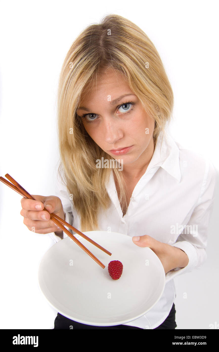 symbol picture 'slimness craze': blond young woman listlessly eating a single raspberry from a plate with chopsticks Stock Photo