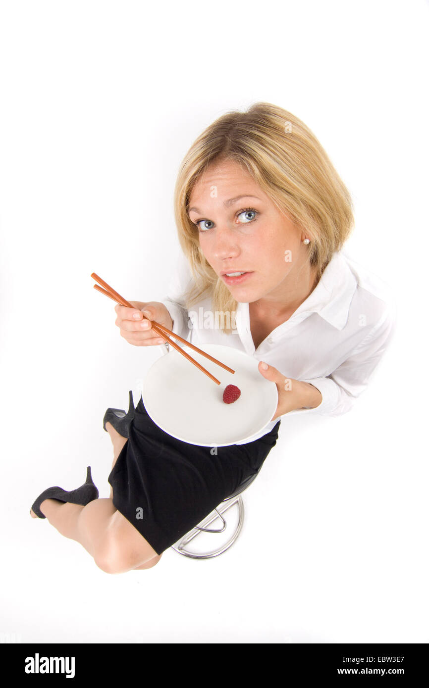 symbol picture 'slimness craze': blond young woman listlessly eating a single raspberry from a plate with chopsticks Stock Photo