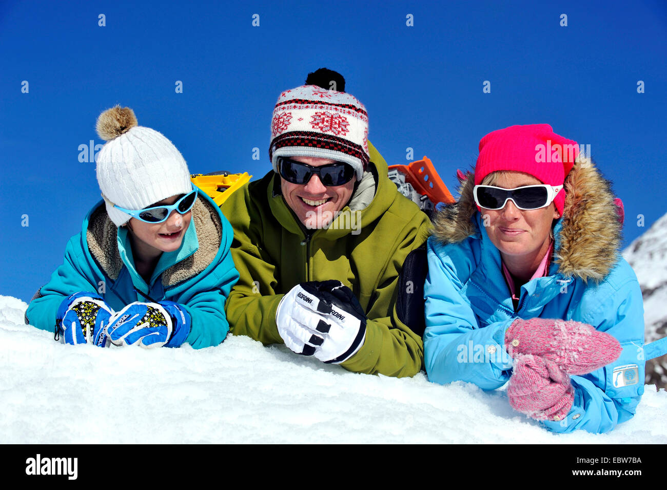family on winter vacation happily lying in the snow side by side on their bellies, France Stock Photo
