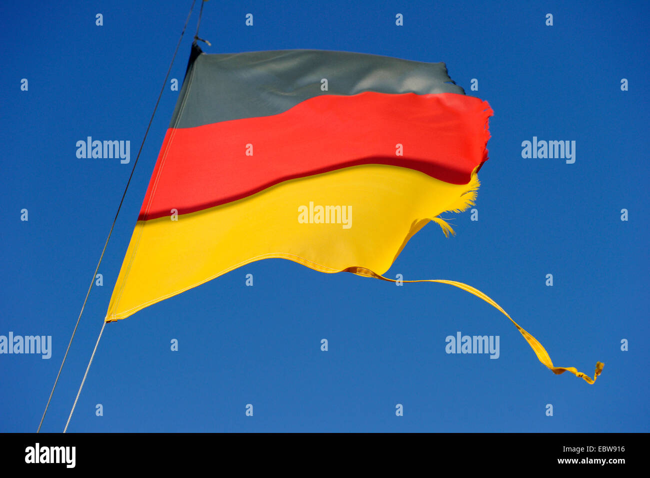German national flag torn in the wind ists waving in front of blue sky Stock Photo