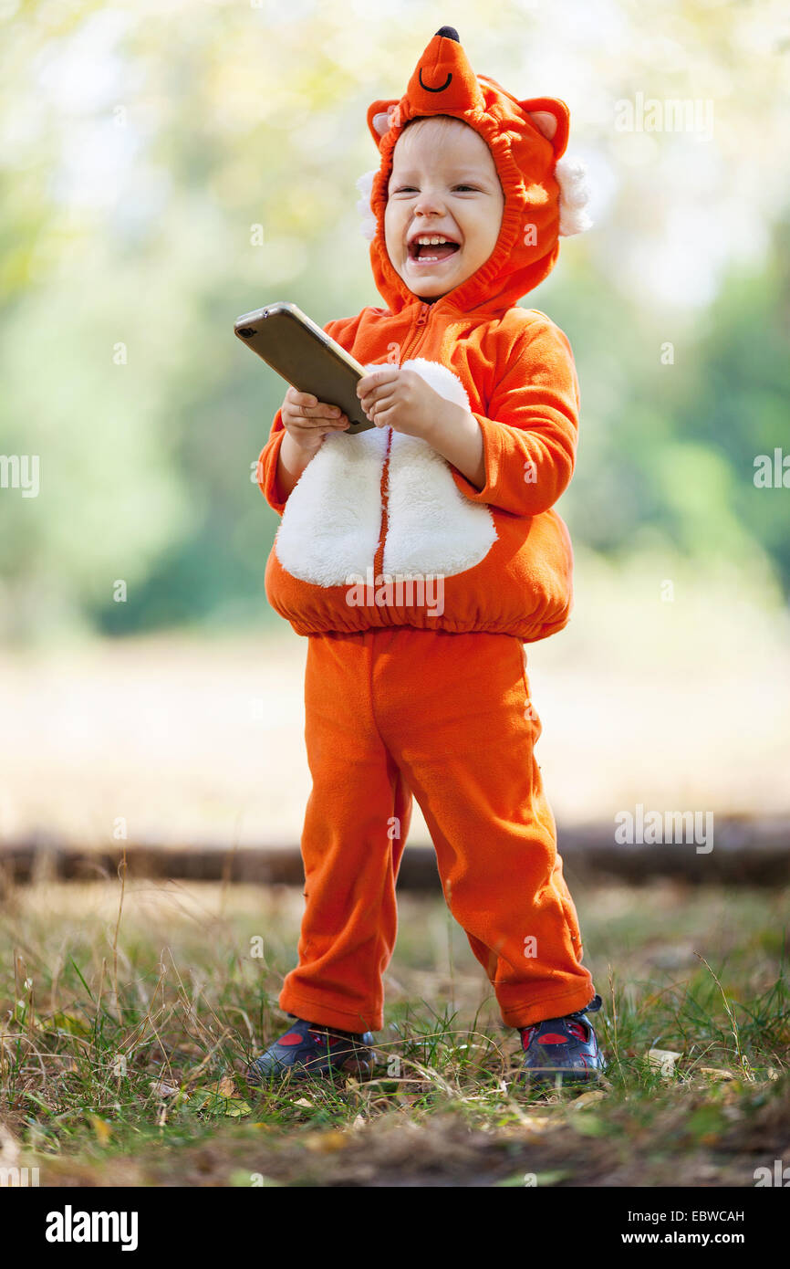 Joyful toddler boy in fox costume holding smartphone Stock Photo