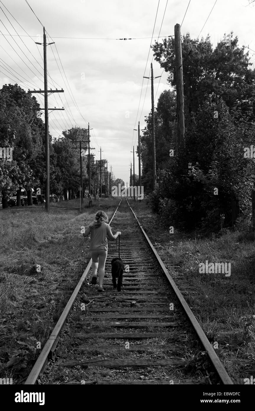Black and white image of a girl and her dog running down railroad tracks Stock Photo