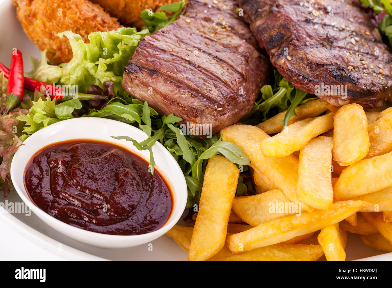 Wholesome platter of mixed meats including grilled steak, crispy crumbed chicken and beef on a bed of fresh leafy green mixed sa Stock Photo