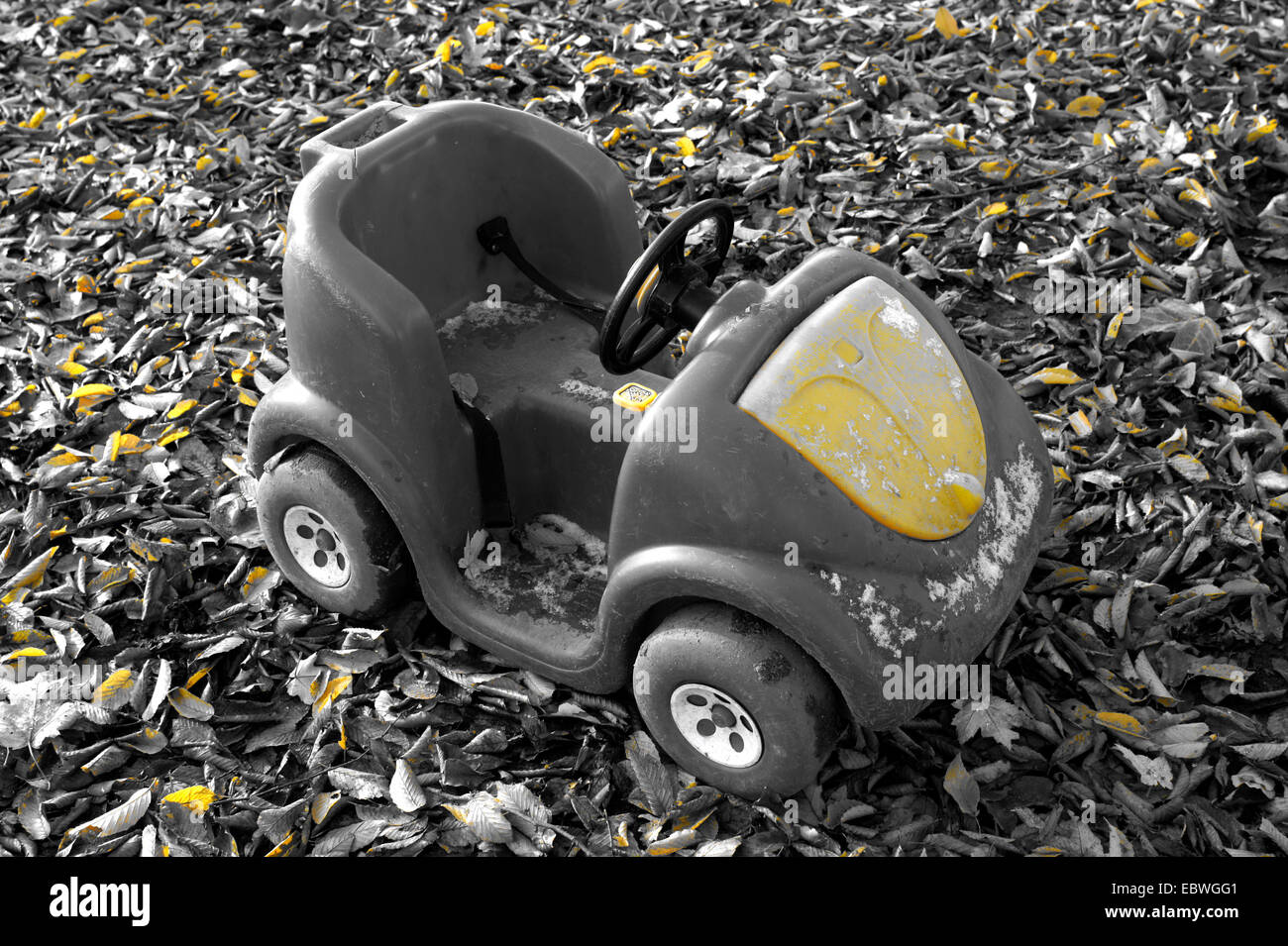 Yellow selective colour image of a child's abandoned toy pedsl car Stock Photo