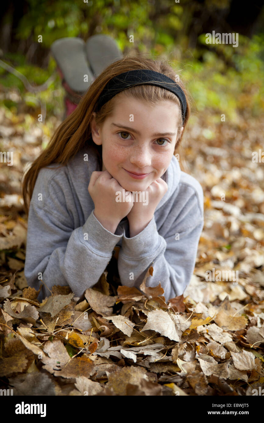 Smiling girl in a vertical portrait outdoors in fall leaves Stock Photo
