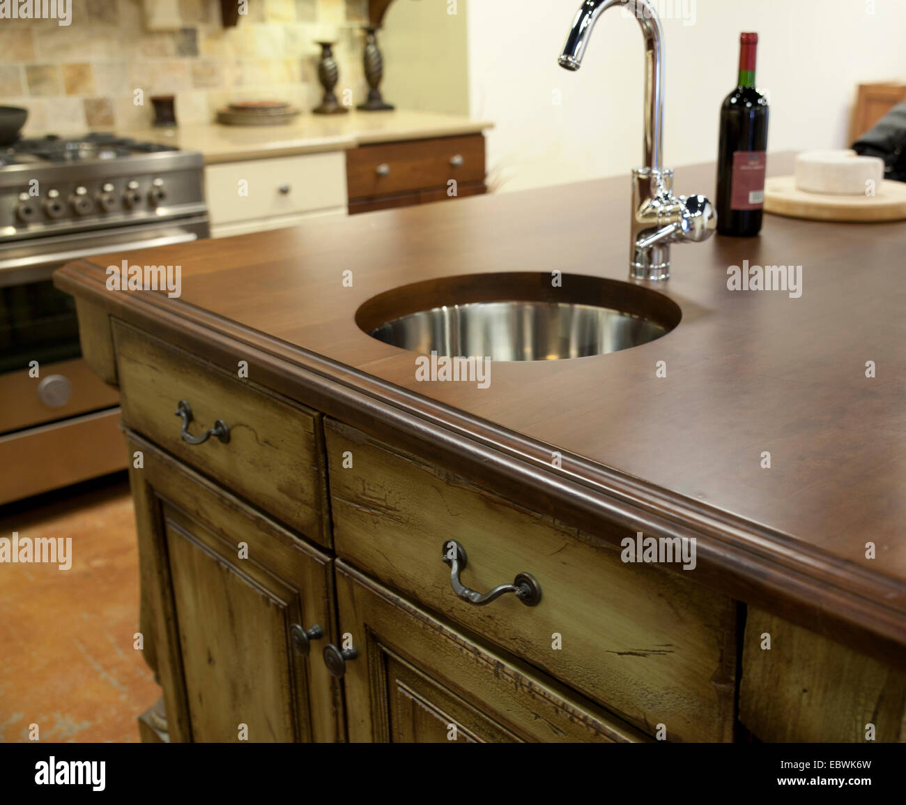 Distressed kitchen cabinets, wooden countertop with modern stainless steel faucet and sink. Stock Photo