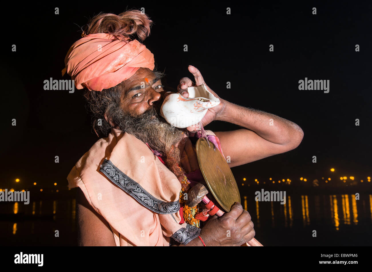 Shiva sadhu, holy man, playing on a shell at night at the Sangam, the confluence of the rivers Ganges, Yamuna and Saraswati Stock Photo