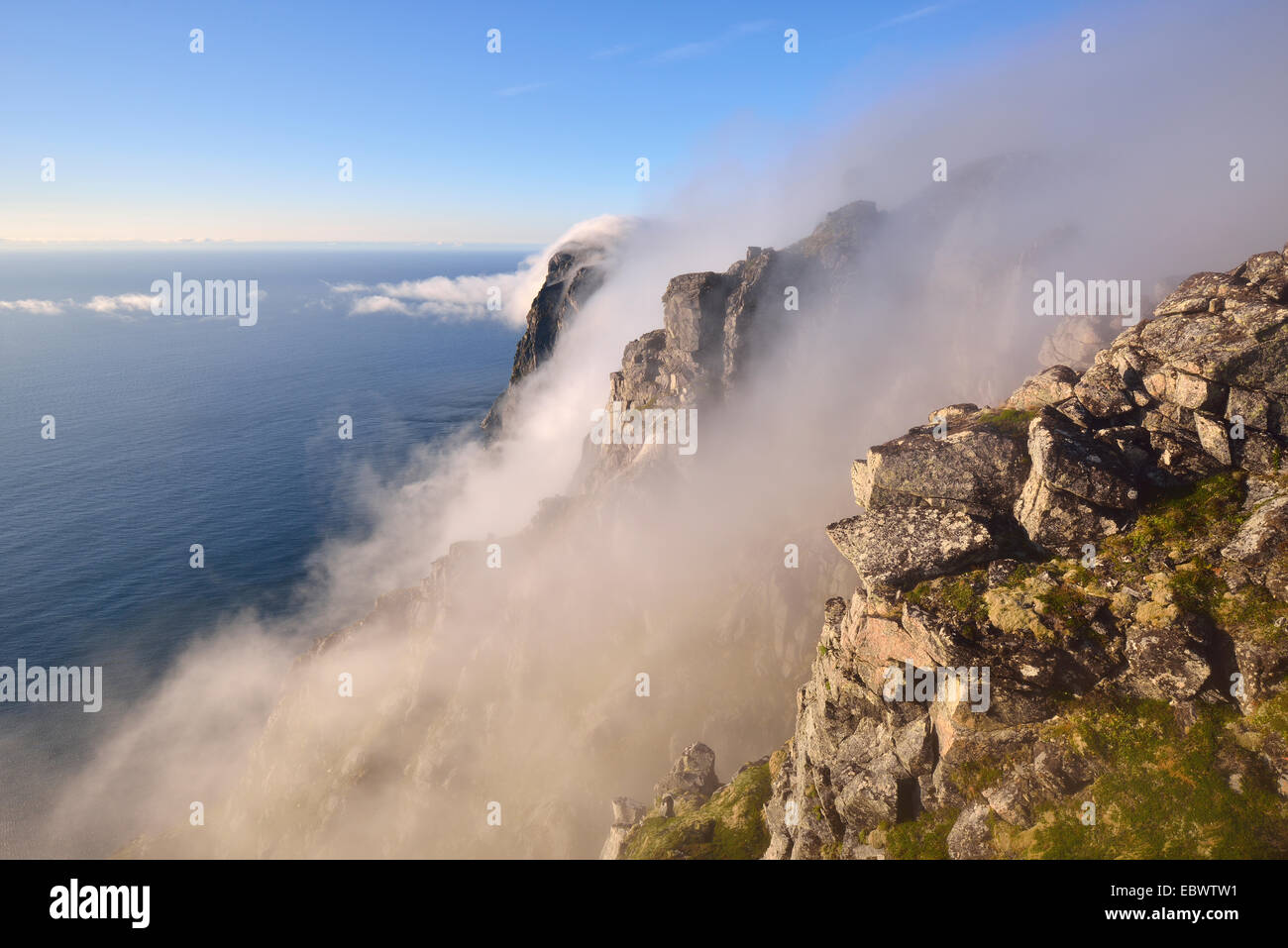 Fog falls down a steep cliff to the sea, mountain Ryten, Moskenesøy Island, Lofoten, Norway Stock Photo