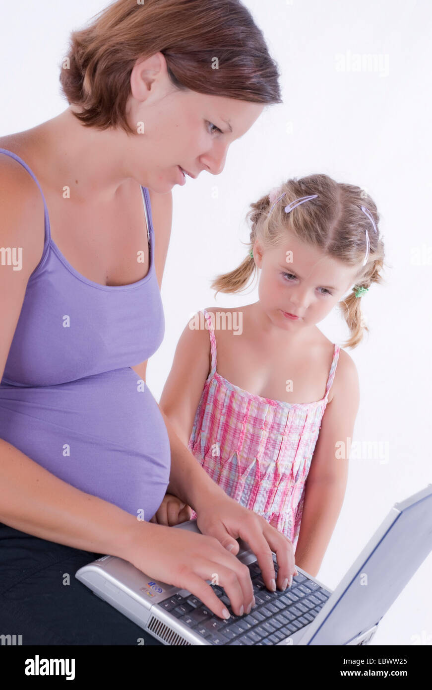 pregnant young woman working on the laptop in her lap, young daughter