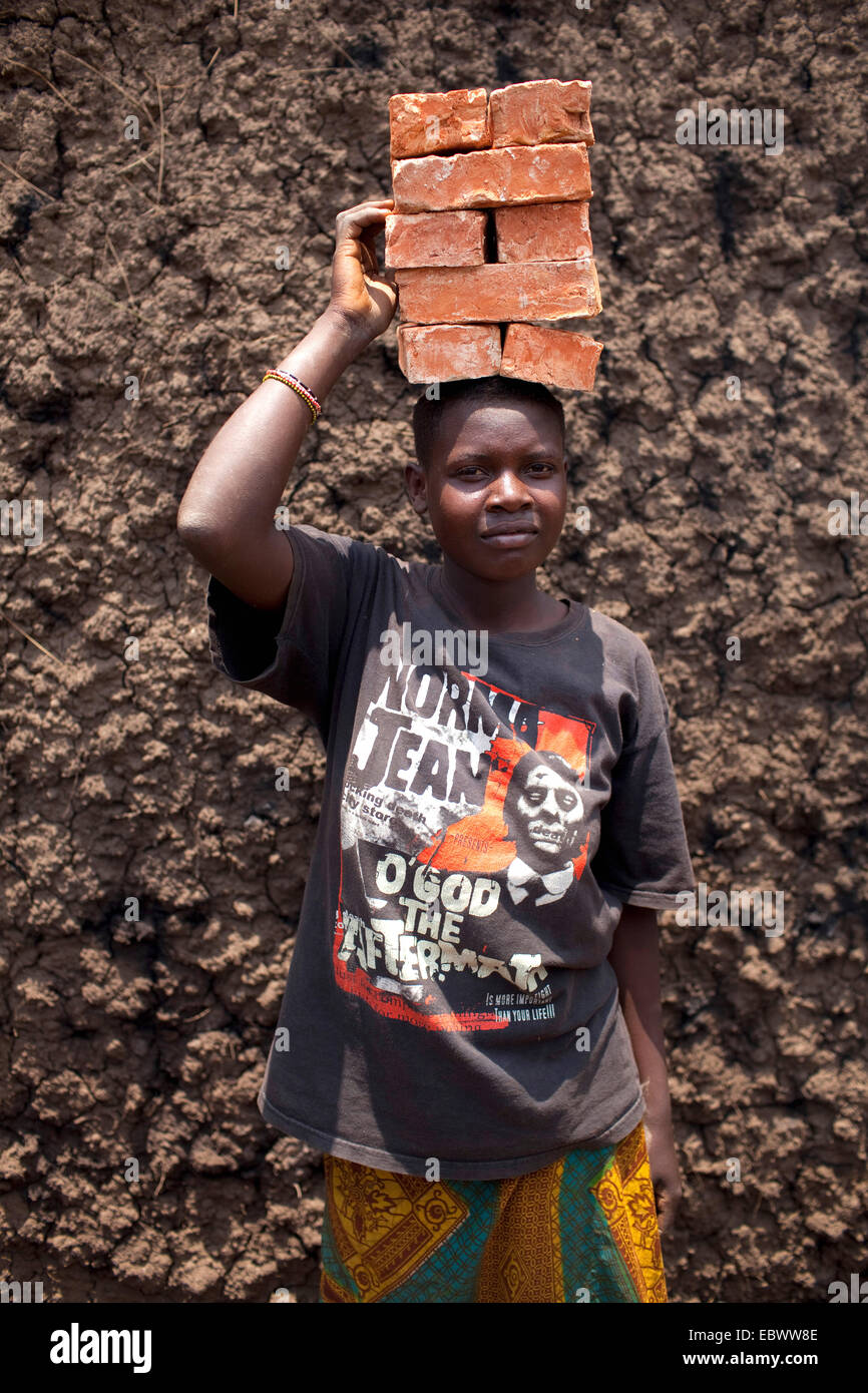 portrait of a boy carrying a stack of bricks on his head which are