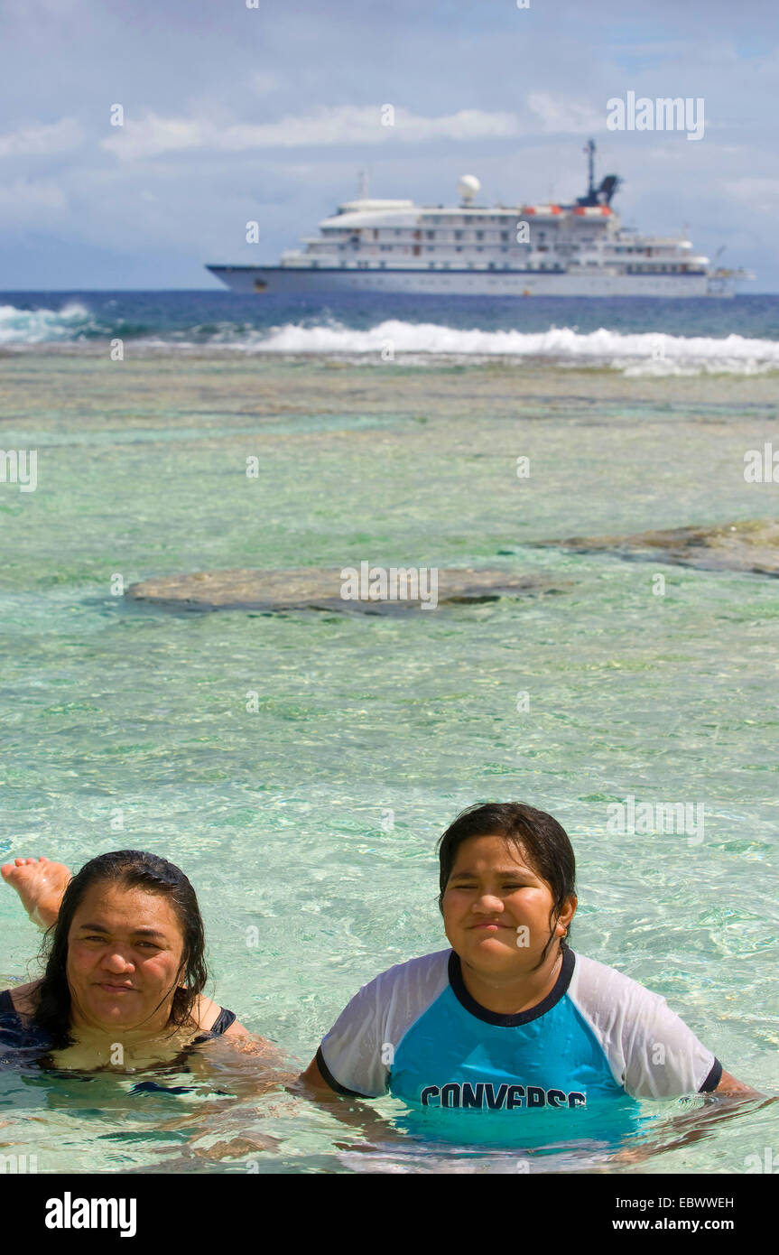 Cruise ship anchored off island with islanders in the water, Cook Islands, Atiu Stock Photo