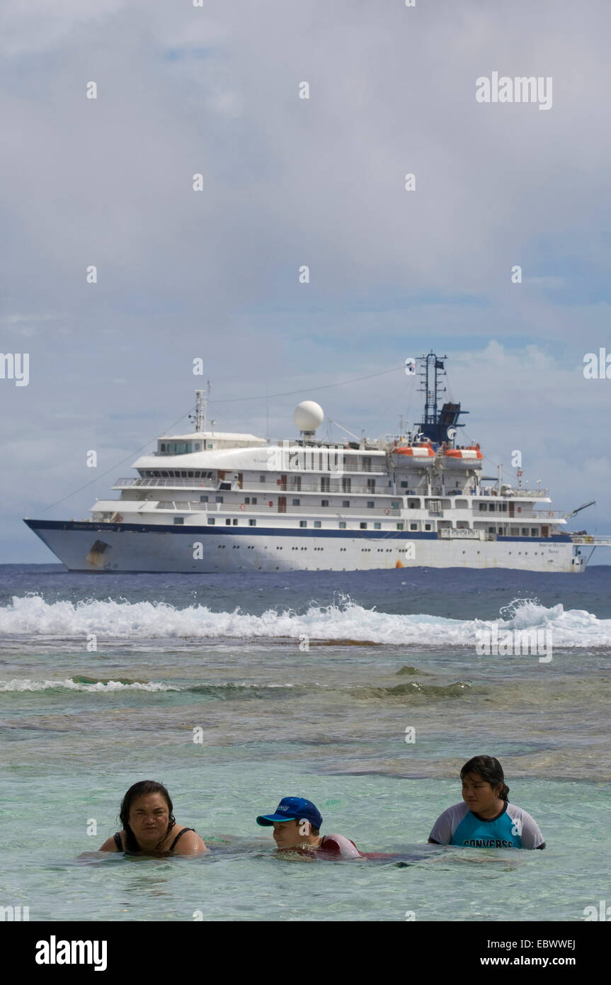 Cruise ship anchored off island with islanders in the water, Cook Islands, Atiu Stock Photo