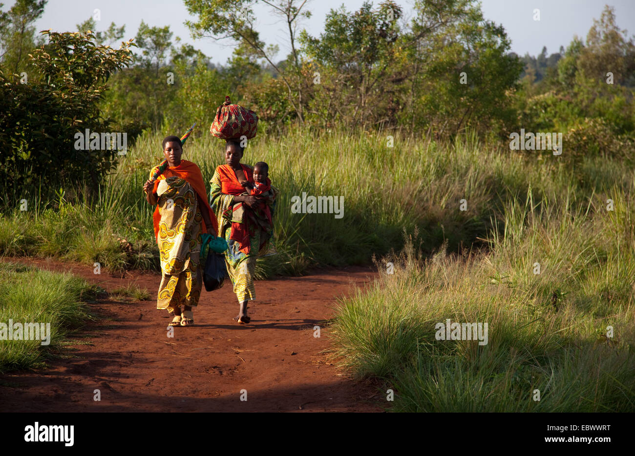two women in traditional clothes walking to the market on a path through a bush landscape, Burundi, Near National Parc de la Ruvubu, Cankuzo Stock Photo