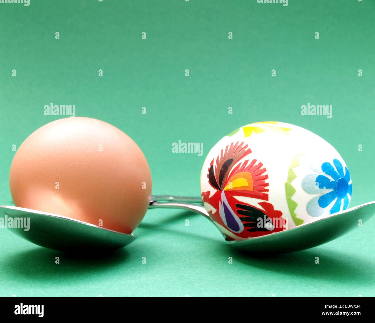 brown egg and colourful painted easter egg lying on spoons Stock Photo