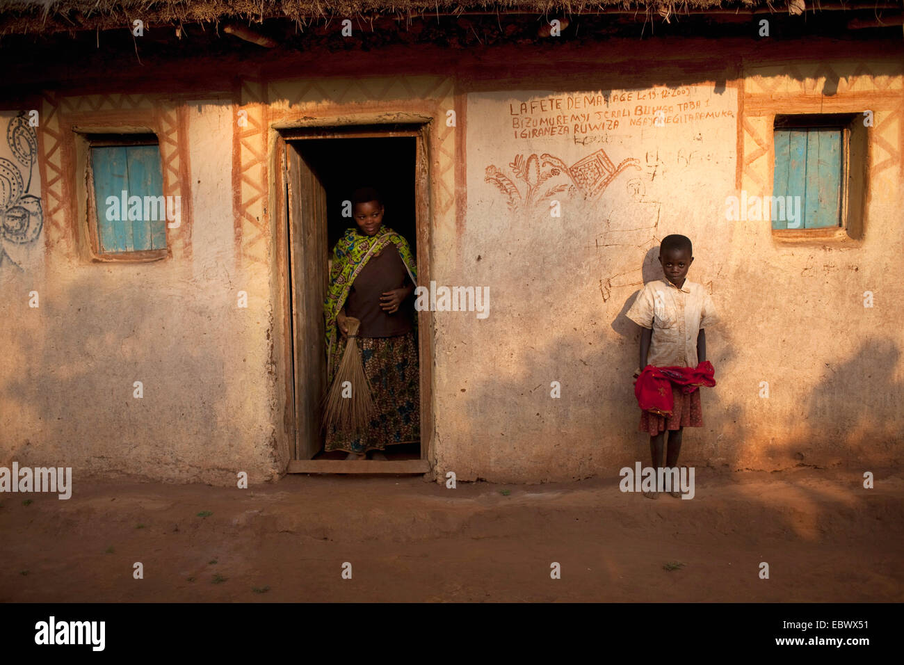 woman with besom standing in entrance, boy leaning against facade, Burundi, Karuzi, Buhiga Stock Photo