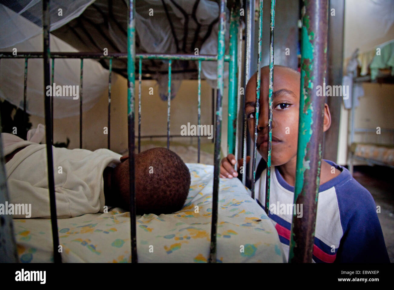 boy sitting beside a bed in which a little girl is sleeping, Burundi, Bujumbura Marie, Bujumbura Stock Photo