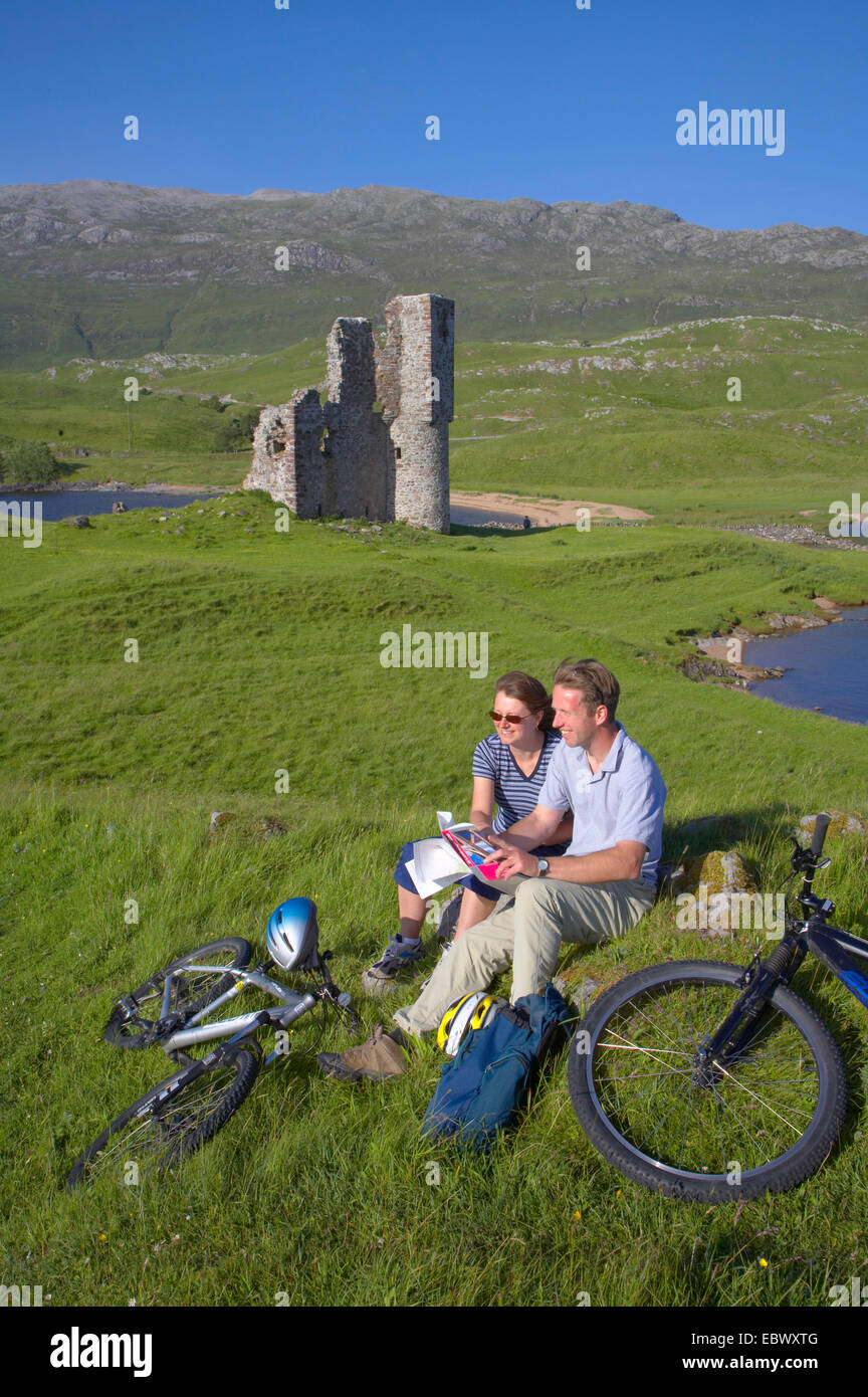 Couple relaxing after bikeride alongside Ardvreck Castle, Loch Assynt, United Kingdom, Scotland, Sutherland Stock Photo