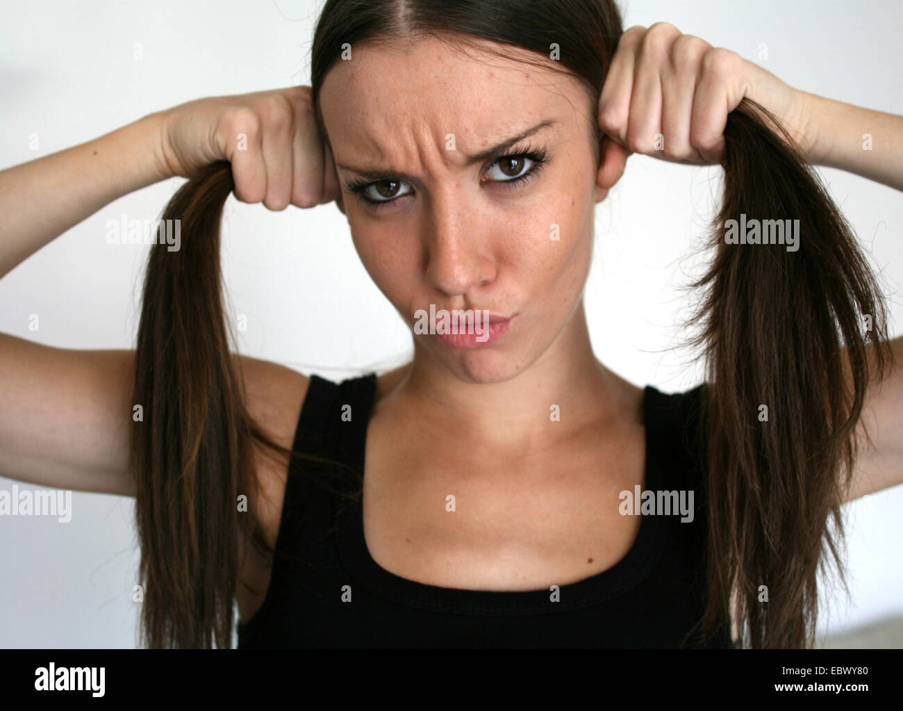 young woman pouting while forming two braits of her brunette long to hair Stock Photo