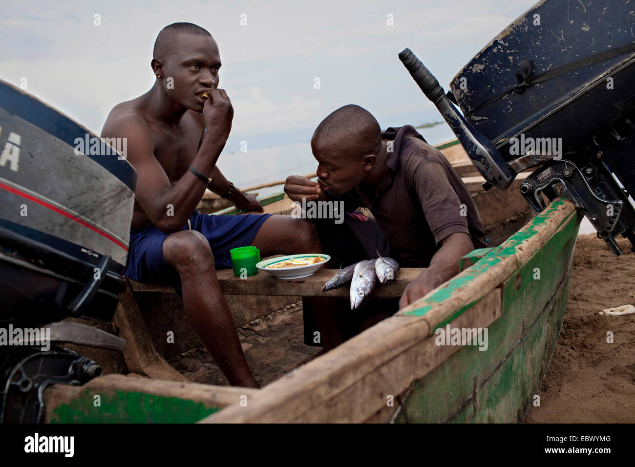 young fishermen sitting in a boat on the sand beach taking their breakfast after a night of work, Burundi, Nyanza Lac, Mvugo, Nyanza Lac Stock Photo