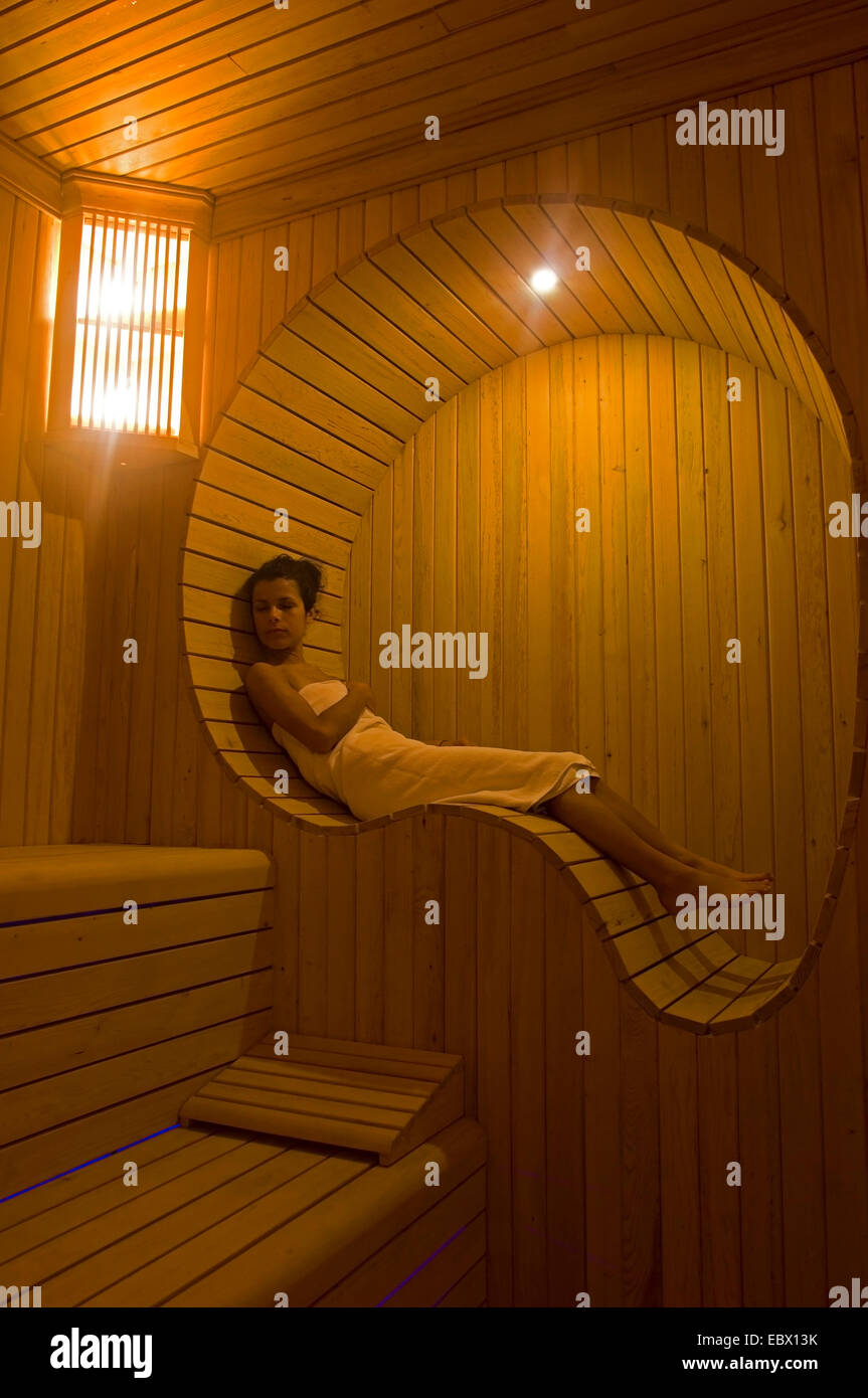 darkhaired young woman resting in the ergonomically formed alcove of a sauna Stock Photo
