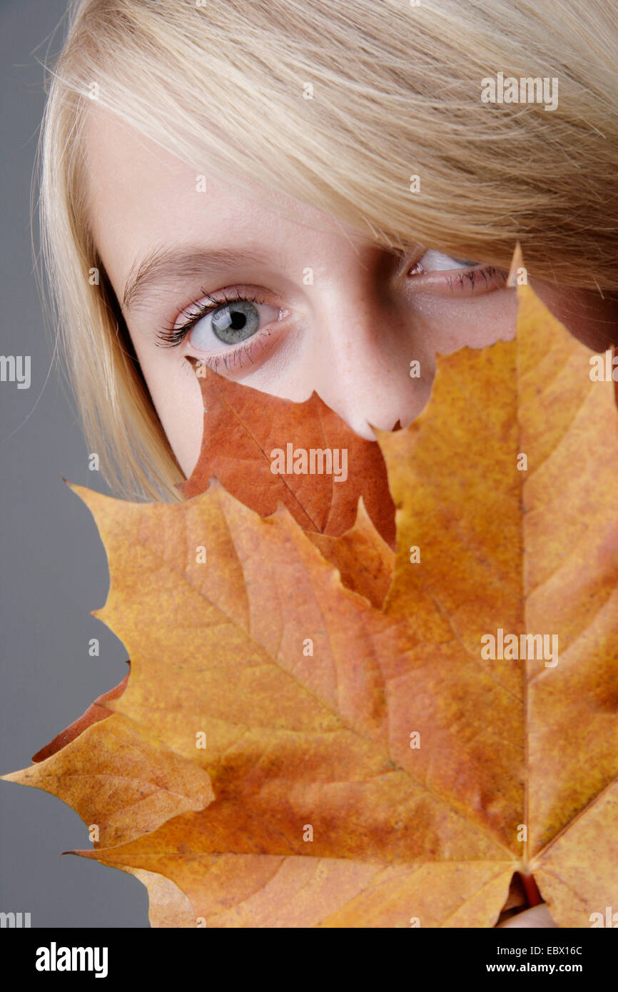 portrait of young blond woman behind autumn leaves, Germany Stock Photo
