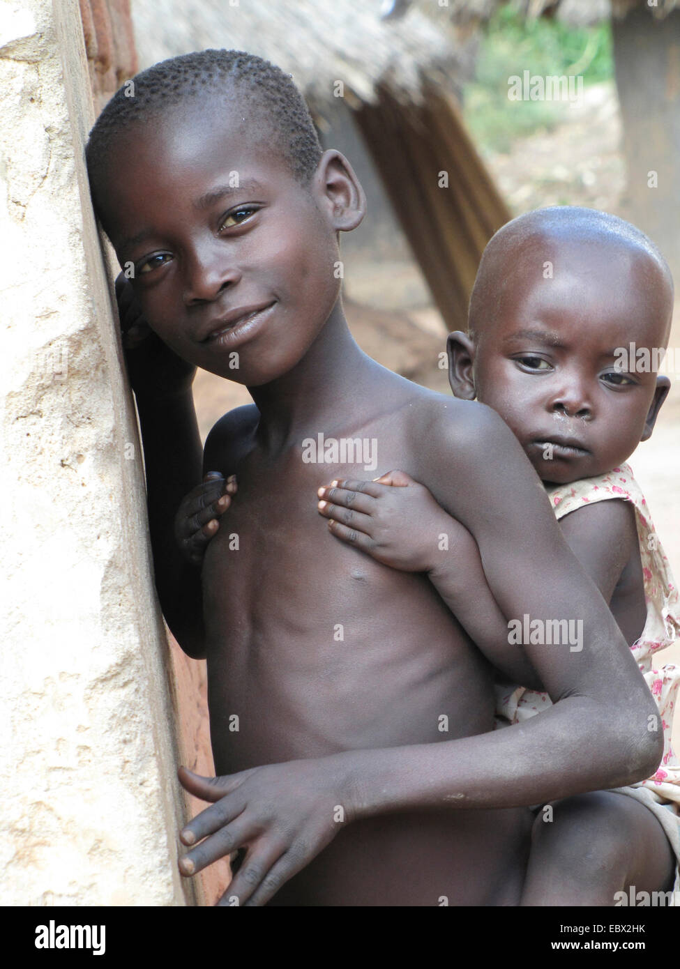 two little children at the refugee camp for internally displaced people in northern Uganda around Gulu, simple mud house in the background, Uganda, Gulu Stock Photo
