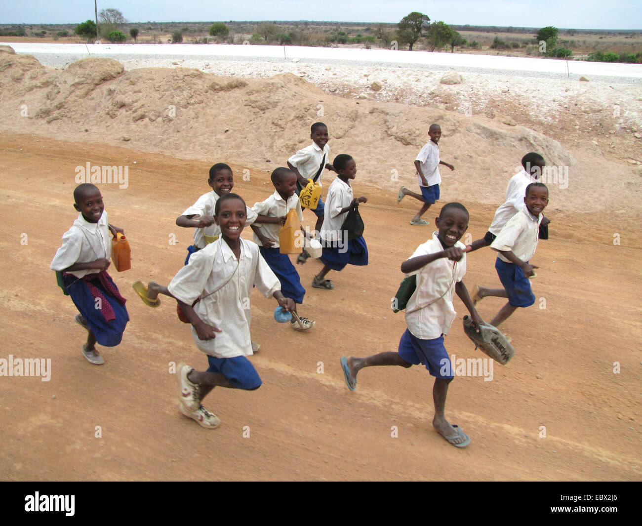 children in school uniforms running on unpaved road with a smile near the administrative capital, Tanzania, Dodoma, Dodoma Stock Photo