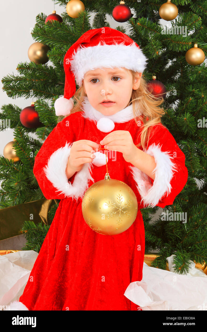 little girl dressed up as Santa Claus with a christmas tree with Christmas tree ball, Switzerland Stock Photo