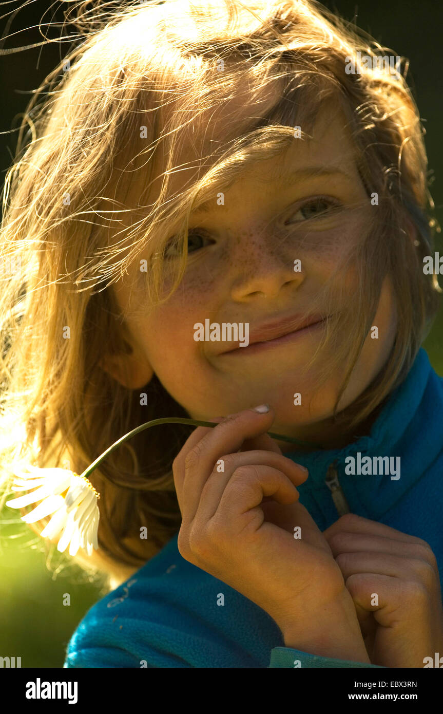 portrait of a smiling 8 year old girl with the hair with her hair and a daisy in her hand waving in the wind, France Stock Photo