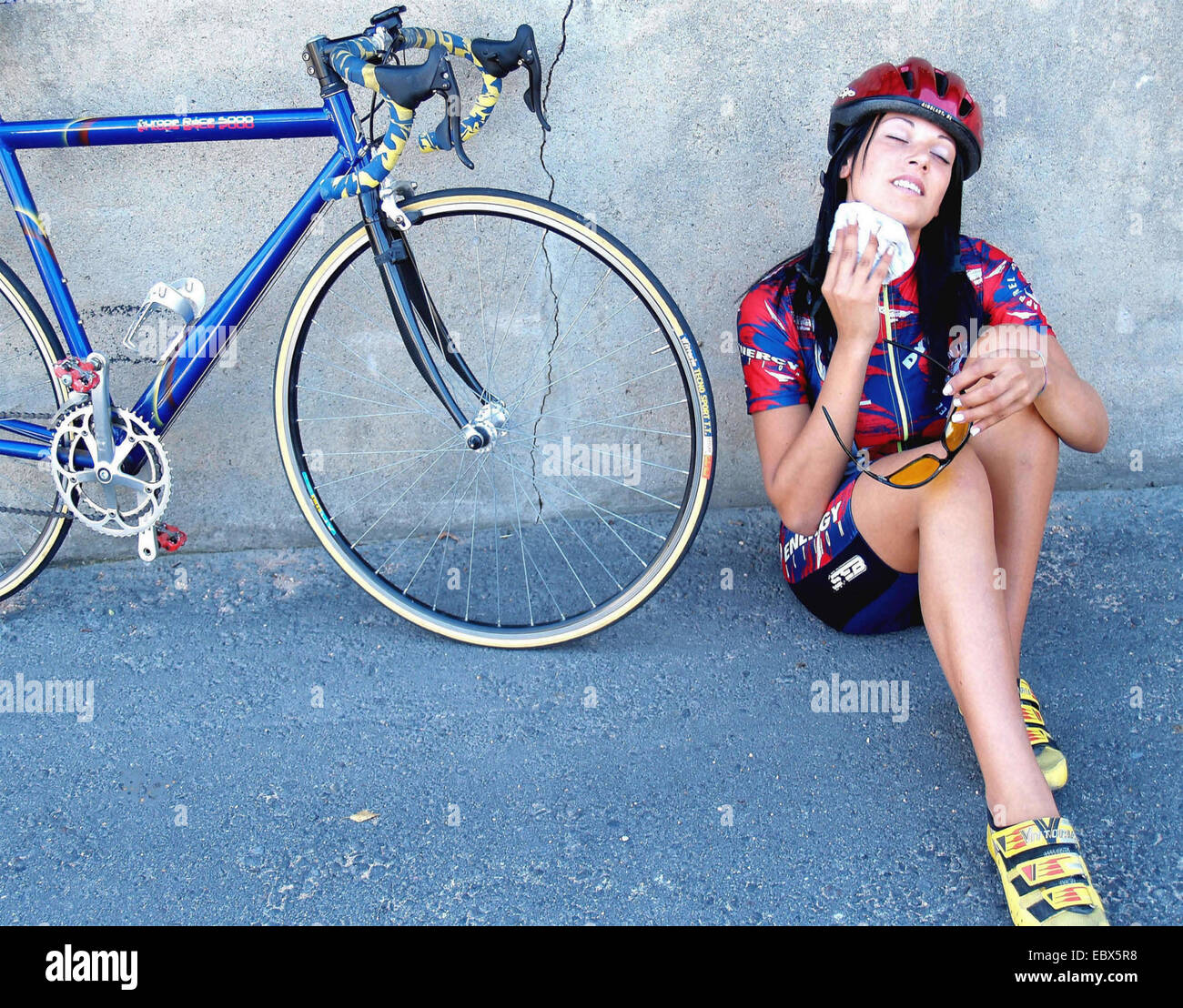 young cyclist sitting on the floor beside her racing bicycle drying her face with a handkerchief Stock Photo