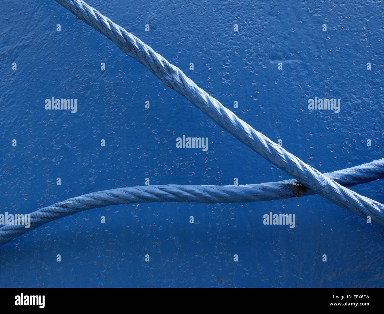 Symbol together and apart, two blue ropes crossing in front of a blue wall Stock Photo
