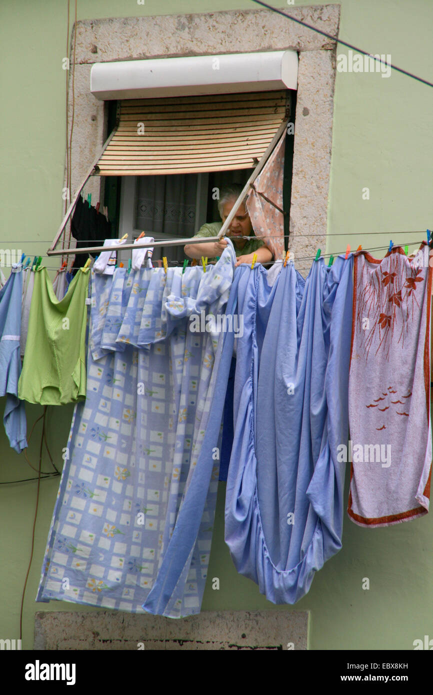 an old woman hanging up laundry on a line in front of her window, Portugal, Lisbon Stock Photo