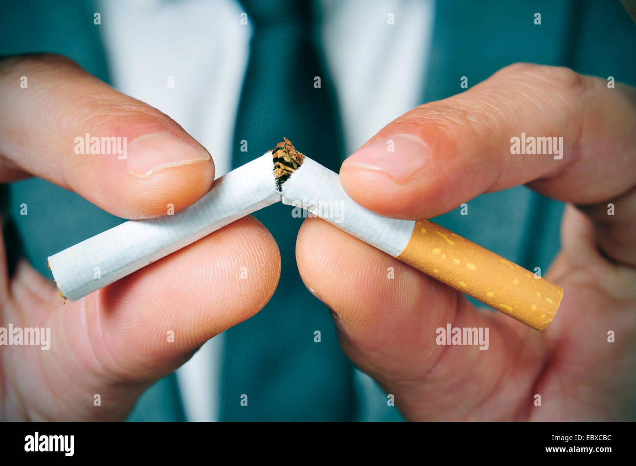 a man wearing a suit breaking a cigarette with his hands Stock Photo