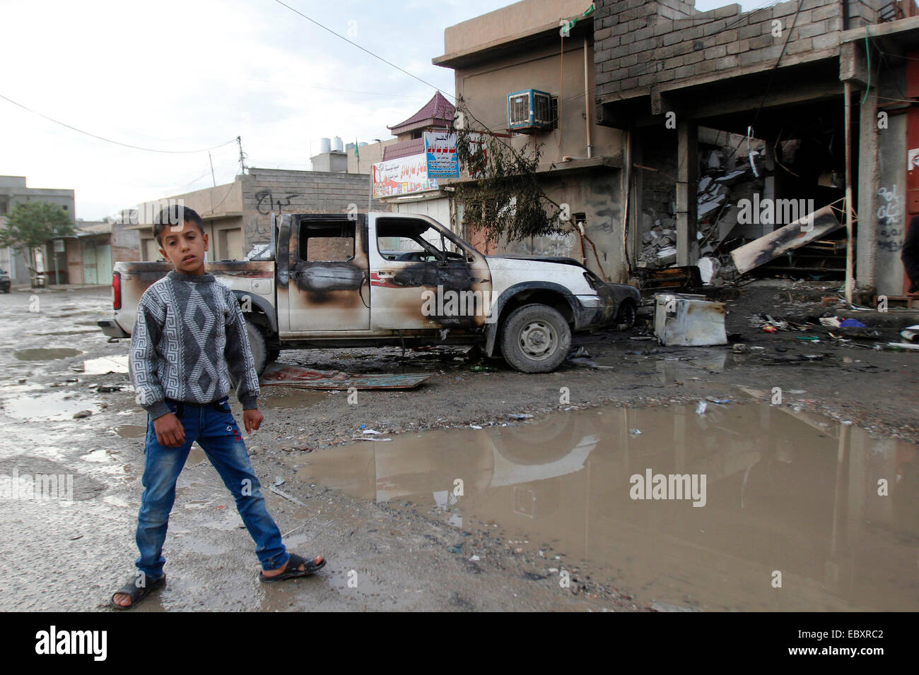 Kirkuk, Iraq. 5th Dec, 2014. A boy stands in front of a damaged car at an explosion site in the city of Kirkuk, Iraq, Dec 5, 2014. A suicide bomber with an explosive vest blew himself up in a cafe in the northern Iraqi city of Kirkuk, killing at least 15 people and wounding 20 others on Dec. 4, a local police told Xinhua on condition of anonymity. © Dena Assad/Xinhua/Alamy Live News Stock Photo