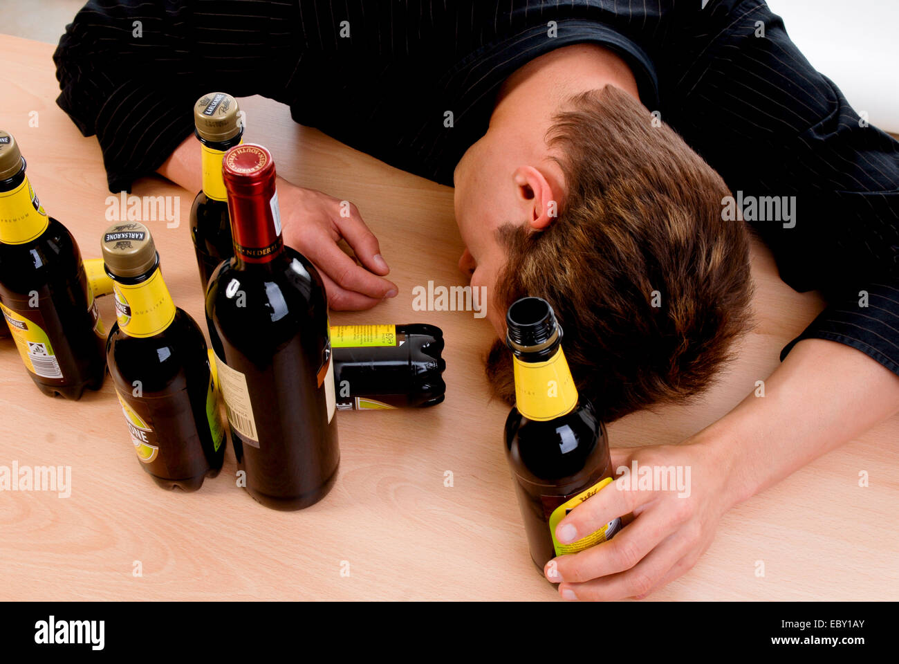 drunken teenager sitting at a desk with beer bottles Stock Photo