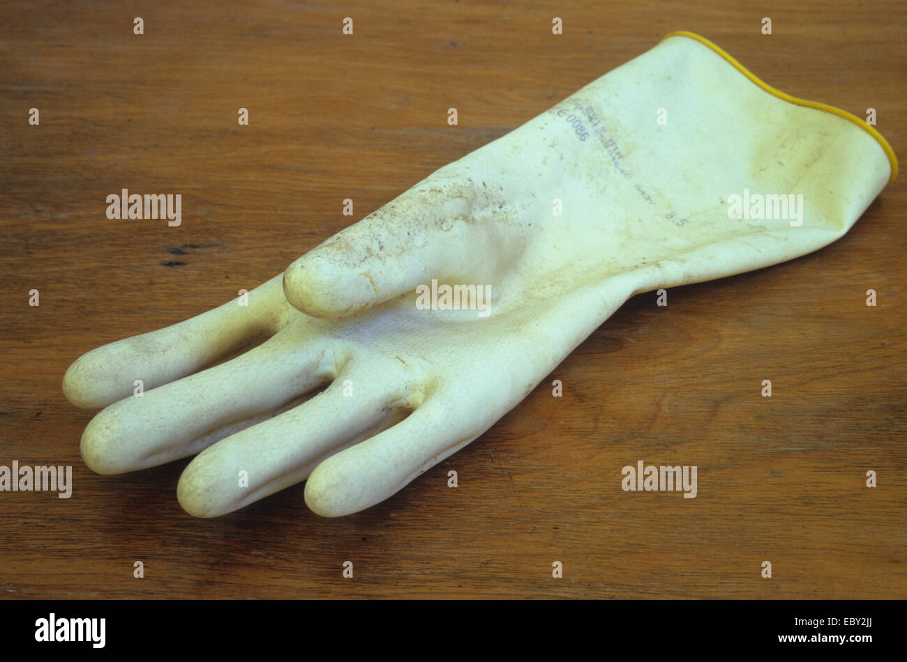 Inside-out yellow rubber glove with stains lying on wooden table Stock Photo