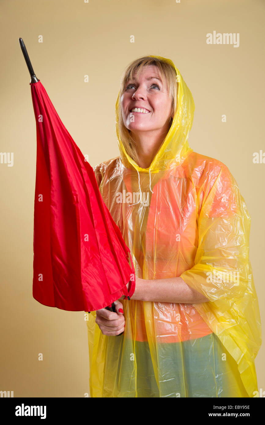 Rain check woman wearing a yellow poncho and holding a red umbrella Stock Photo