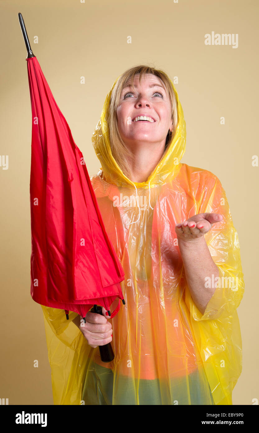Rain check woman wearing a yellow poncho and holding a red umbrella Stock Photo
