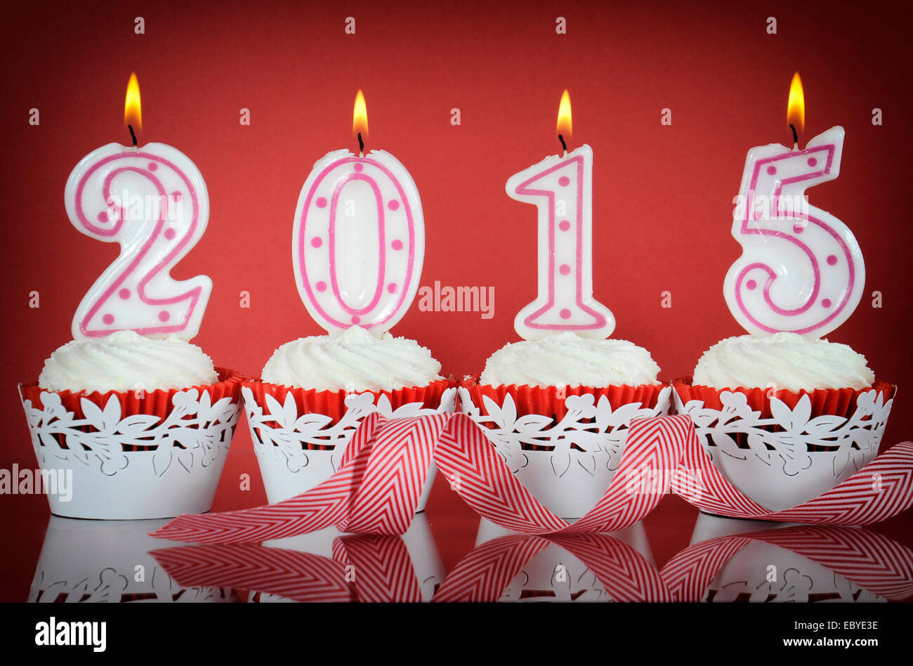 Happy New Year for 2015 red velvet cupcakes in red and white theme with lit candles on a red background. Stock Photo