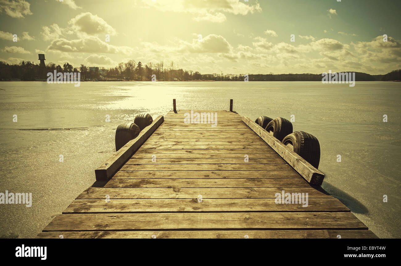 Vintage retro toned image of a pier on frozen lake. Stock Photo